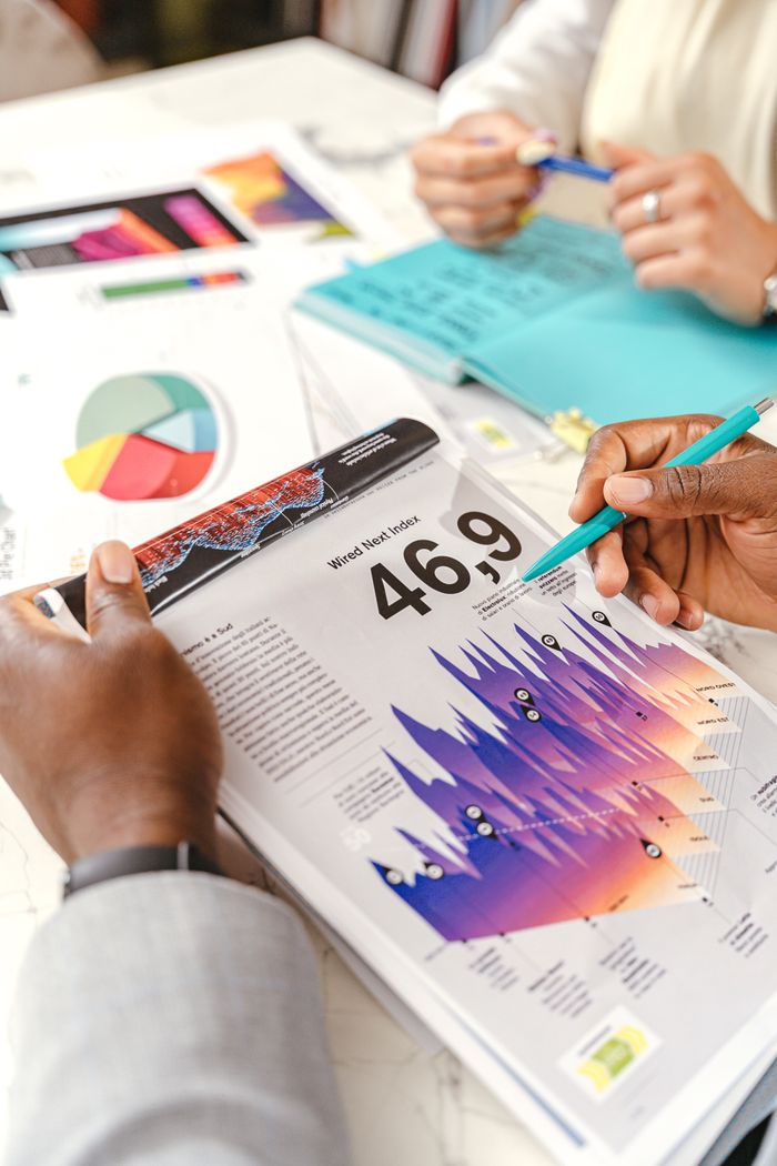 Des mains échangent autour de graphiques de données colorés pendant une réunion d’affaires, avec des documents et des schémas.